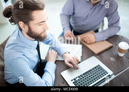 High angle view of young businessman sitting at the table and typing on laptop Stock Photo
