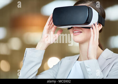 Young attractive Caucasian woman in business attire having fun in virtual reality goggles on blurred background, lens flare Stock Photo