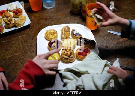 close up of a plate of kid’s hand picking delicious fresh mini french cakes and pastries off a plate during a party Stock Photo
