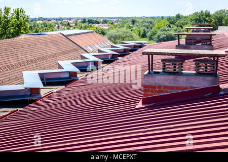 Chimney made of bricks for heating and ventilation on the colored corrugated metal roof. Stock Photo