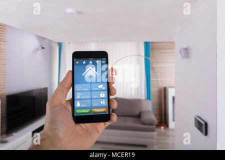 Close-up Of Human Hand Using Smart Home System On Smartphone In Living Room Stock Photo