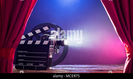 Illuminated Movie Camera With Clapperboard And Film Reel Against Colored Background Stock Photo