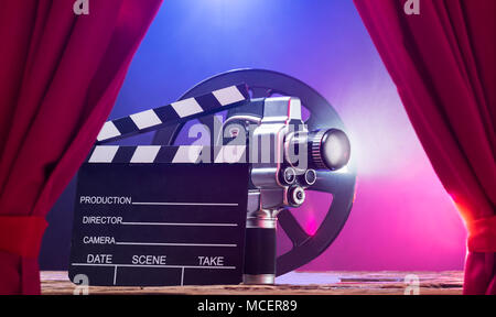 Illuminated Movie Camera With Clapperboard And Film Reel Against Colored Background Stock Photo