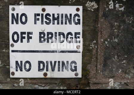 Old weathered No fishing off bridge No diving sign screwed on to old stone wall Stock Photo