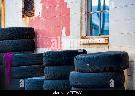 Tires stacked against a building with a red rag hanging off of one stak. Stock Photo