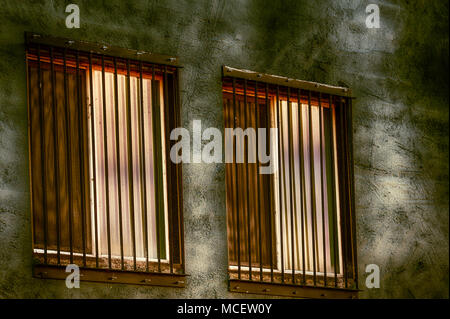 Barded windows reflecting filtered sunlight from a nearby tree not seen in the scene but leaving patterns of shade on the building Stock Photo