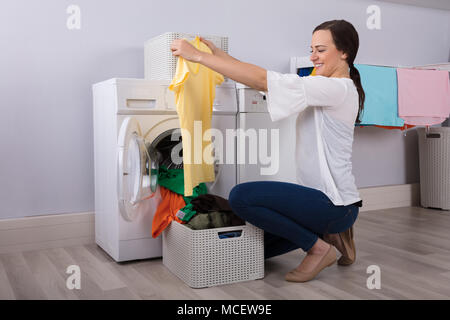 Happy Young Woman Looking At Cleaned Yellow Tshirt After Washing In Washing Machine Stock Photo