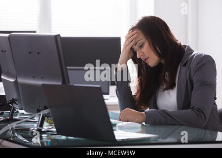 Stressed Young Businesswoman With Hand On Head Sitting At Workplace Stock Photo