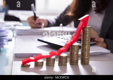 Increasing Golden Coins With Red Arrow Showing Upward Direction In Front Of Businessperson Calculating Bill Stock Photo