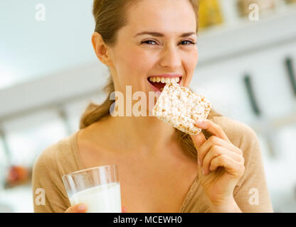 Happy young woman eating crisp bread with milk in kitchen Stock Photo