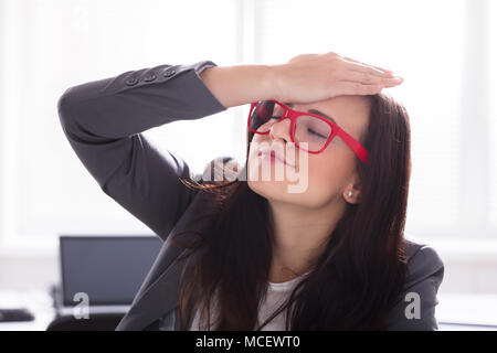 Young Businesswoman With Her Hand On Forehead Wearing Red Spectacles Stock Photo