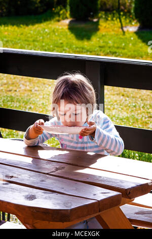 Little girl  lapping her milk soup directly from plate , outdoors. Stock Photo