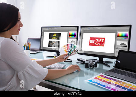 Female Designer Holding Color Swatch Working With Gift Card On Computer Screen Stock Photo