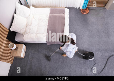 Happy Young Housekeeper Cleaning Carpet With Vacuum Cleaner In Hotel Room Stock Photo