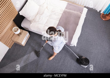 High Angle View Of A Young Female Janitor Cleaning Carpet With Vacuum Cleaner Stock Photo