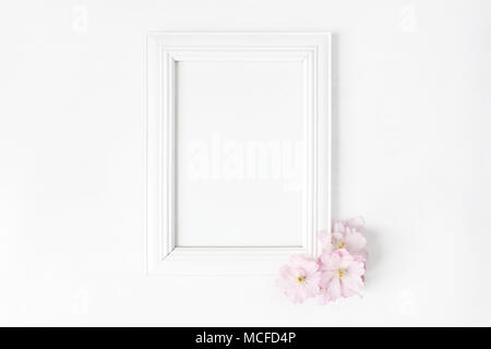 White blank wooden picture frame mockup with pink Japanese cherry blossoms lying on the white table. Poster product design. Styled stock feminine phot Stock Photo