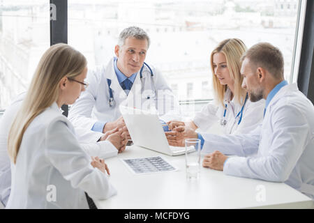 Clinic, people, healthcare and medicine concept - group of medics with brain x-ray scan and laptop at hospital office Stock Photo
