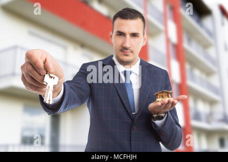 Handsome realtor holding house and giving apartment keys as new home offer concept on flat building backgound Stock Photo