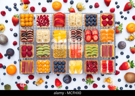 Colourful square fruit tarts on a wire cooling rack against a white background Stock Photo