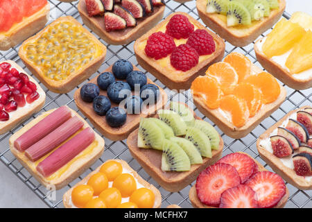 Colourful square fruit tarts on a wire cooling rack against a white background Stock Photo