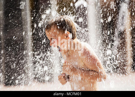 A boy playing with water in park fountain. Hot summer. Stock Photo