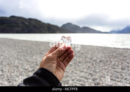 Male hand holding Piece of ice that was broken off from iceberg and found during low tide near Gray Glacier, Torres Del Paine, Chile. Stock Photo