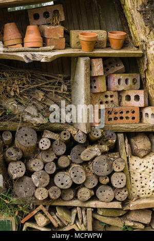 Insect hotel or bug house made with old logs bricks and clay pots to provide shelter and a nesting or hibernation site for bees and insects Stock Photo