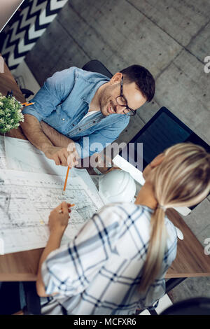 Young successful architect colleagues analyzing blueprints and talking about him at the office. Stock Photo