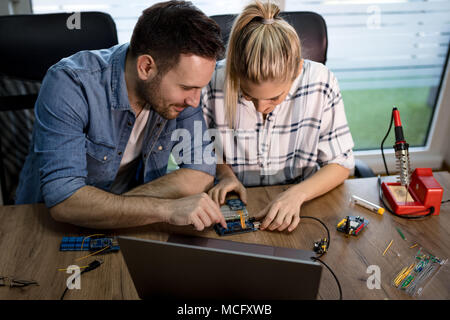 Man helping woman soldering elements of circuit board. Stock Photo