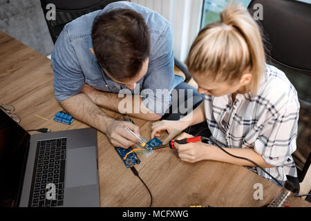 Top view on two engineers who soldering elements of circuit board. Stock Photo
