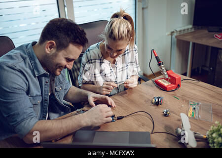Man helping young woman soldering elements of circuit board. Stock Photo