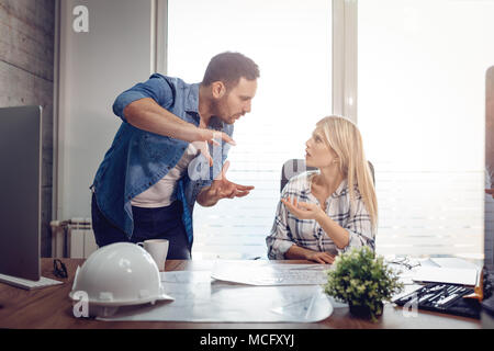 Young worried architect colleagues talking and analyzing blueprints while working on a new project at the office. Stock Photo
