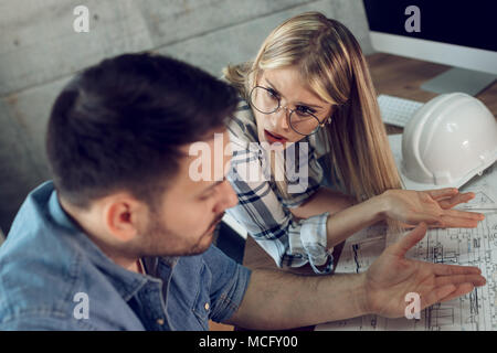 Young worried architect colleagues talking and analyzing blueprints while working on a new project at the office. Stock Photo