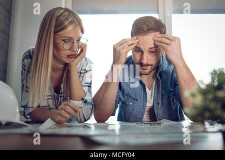 Young worried architect colleagues analyzing blueprints while working on a new project at the office. Stock Photo