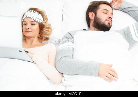 Woman using laptop in bed while her husband is sleeping next to her Stock Photo