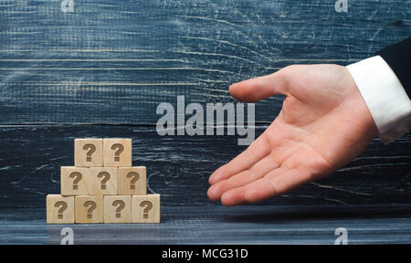 The outstretched hand of a businessman points to a pyramid of wooden squares with the symbols of the question mark. Concept promoter, sale and purchas Stock Photo