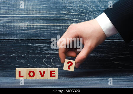 The hand stretches a cube with the question mark symbol to the word love. The concept of love and love relationships, loyalty and feelings. Young coup Stock Photo