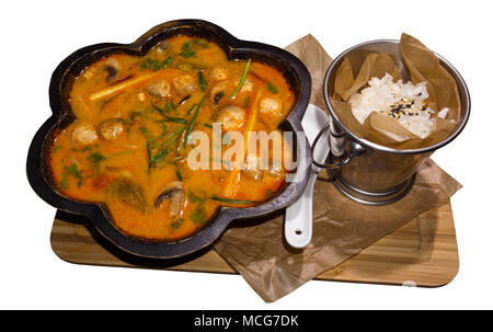 hot Thai soup tom yum (or tom yam) in a curly wooden plate and a bucket of rice served on a board isolated on a white background Stock Photo