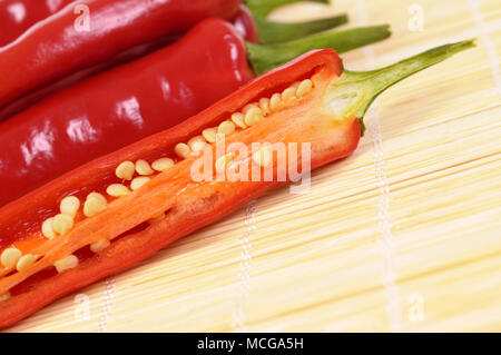 Red chili peppers cut half inside showing seeds on a bamboo asian mat Stock Photo