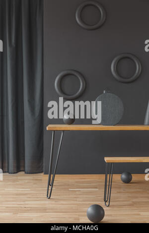 Wooden hairpin table and a matching bench in black dining room interior with circular wall decoration Stock Photo