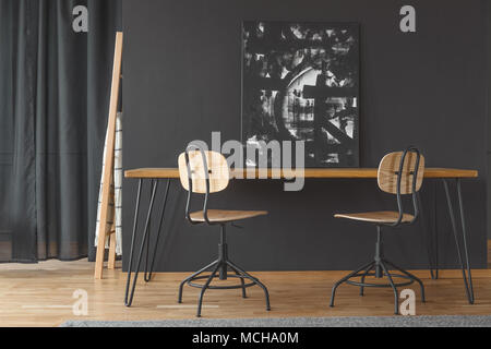 Black and white painting standing against a dark wall, on a wooden dining table in monochromatic room interior Stock Photo