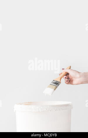 cropped image of woman holding brush in white paint above bucket isolated on white Stock Photo