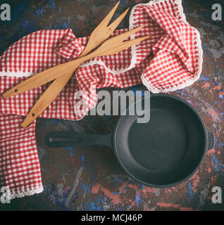 empty round black cast-iron frying pan with a handle and two wooden forks on a brown background, top view Stock Photo