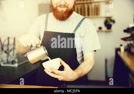 Coffee Business Concept - handsome bearded man in apron making coffee while standing at cafe Stock Photo