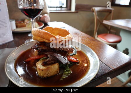 A lovely Sunday Roast in a classic British pub. Roast beef topside with season vegetables, Yorkshire pudding and a glass of Malbec red wine. Stock Photo