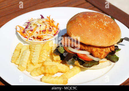 A delicious crispy fish burger with cheese, lettuce, and mayonnaise with french fries and salad onside. Stock Photo