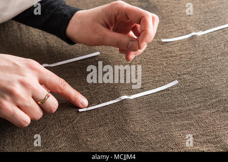 Restoration studio, restorer, hands sewing finished support fabric on lent scarf at paper strip marking, Munich, Bavaria Stock Photo