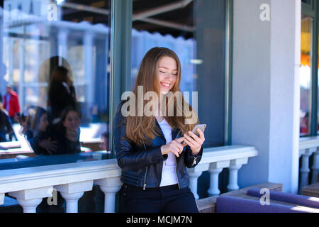 Young woman chatting by smartphone at street cafe. Stock Photo