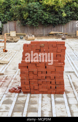 Pile of typical red house bricks stacked on a partly built new housing infill development construction site in southeast England, Surrey, UK Stock Photo