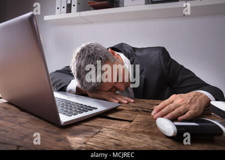 Businessman Sleeping In Office With Laptop On Wooden Desk Stock Photo